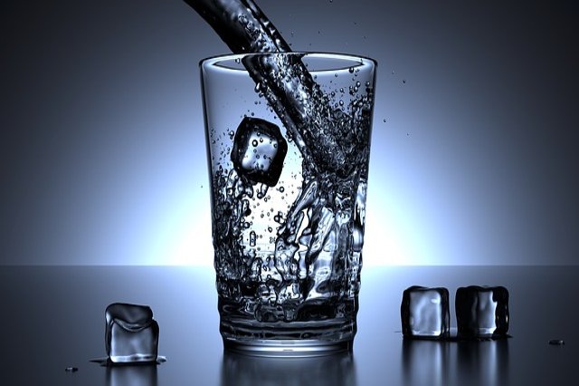 Vaso de agua con hielo recibiendo un chorro de agua.